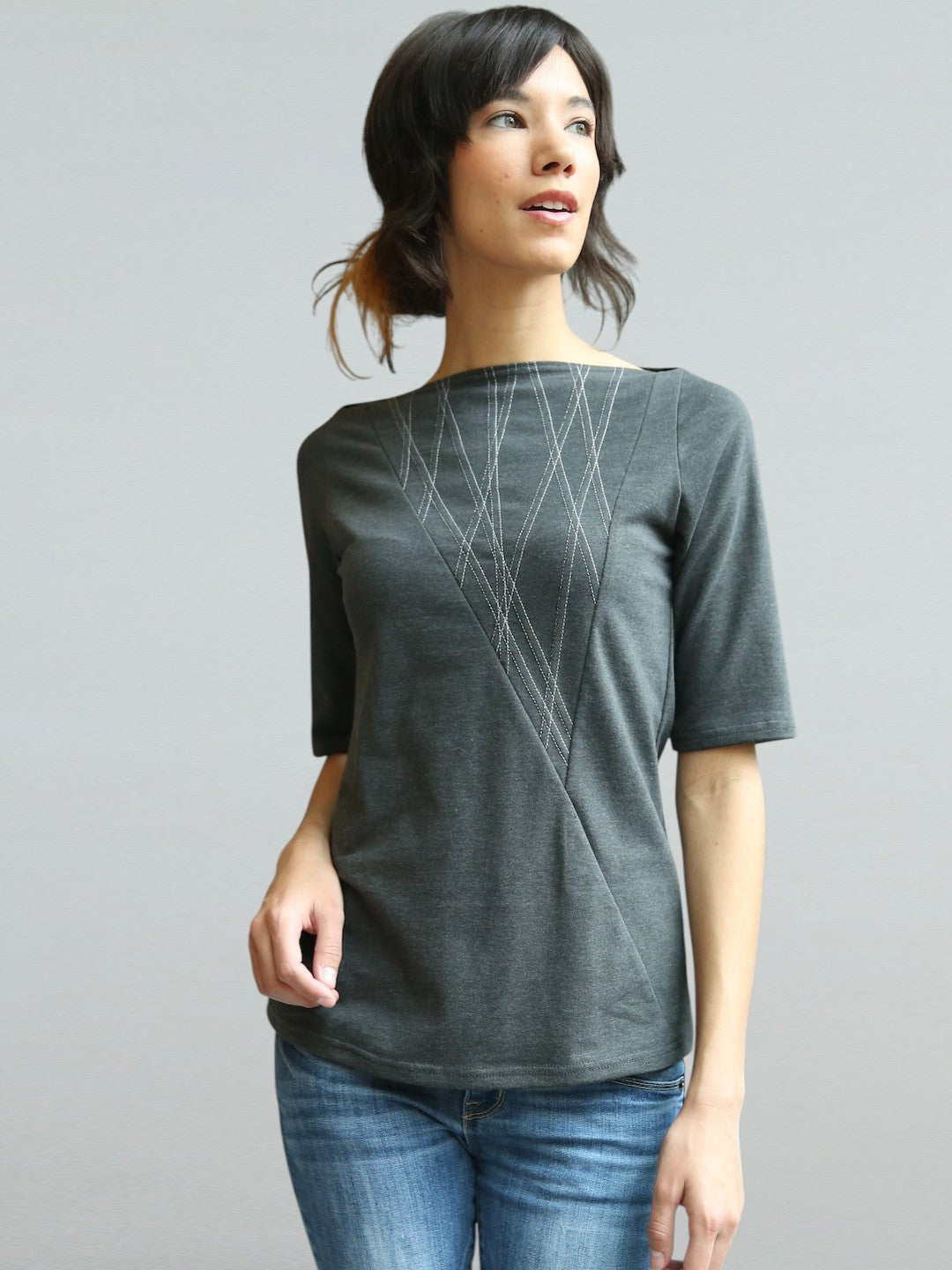 Woman wearing a gray t-shirt with geometric design on a plain background